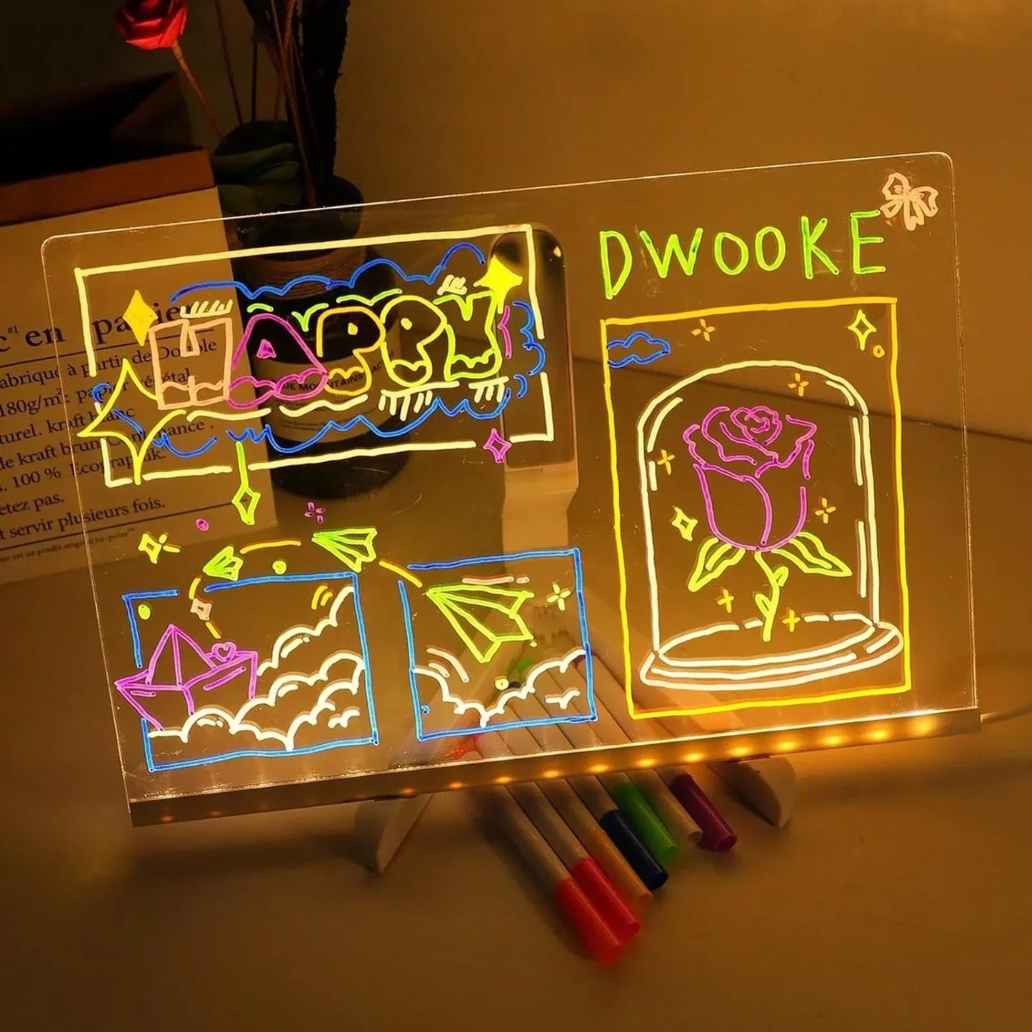 Transparent board with colorful drawings and text, illuminated by LED lights, on a wooden surface.